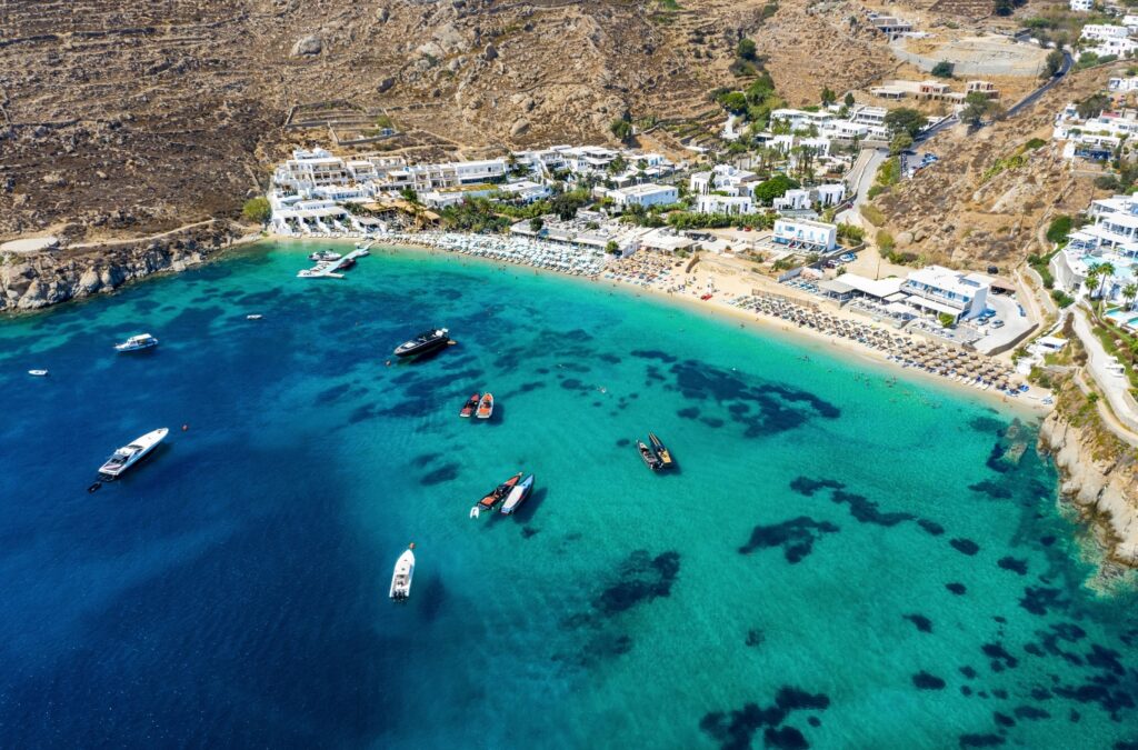 Aerial view of a turquoise bay in Greece with yachts anchored along the coastline.