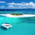 Aerial view of a luxury charter catamaran anchored near Sandy Spit, a small tropical island with white sandy beaches and turquoise waters in the British Virgin Islands.