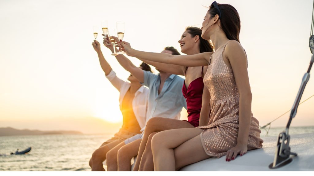 a lively group of friends enjoying a champagne party aboard a luxury catamaran yacht. Set against the backdrop of a serene summer sunset, the scene showcases a diverse group celebrating their holiday vacation with laughter, toasts, and breathtaking views. Perfectly illustrating the joy and elegance of a yacht charter experience, this moment encapsulates the ultimate winter getaway.